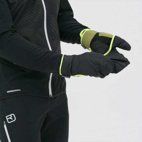 Ortovox Fleece Grid Handschuhe Eine Person trägt Ortovox Fleece Grid Cover Handschuhe in Schwarz und Grün. Der Cover Hoody ist über die Finger gezogen.
