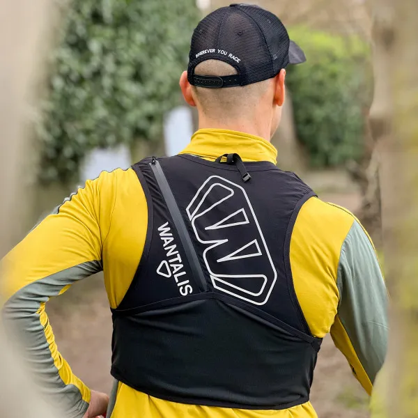 Läufer mit Hydrabag Elite 8L Trinkweste von hinten, schwarze Kappe mit Aufdruck, gelbes Langarmshirt, Blick in die Natur.