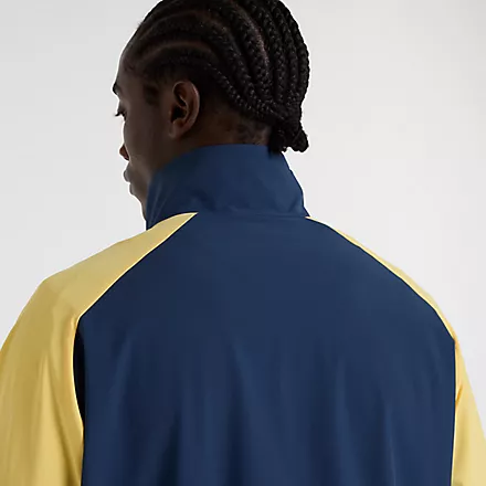 Nahaufnahme einer New Balance In Game Woven Track Jacket in Navy/Gelb, getragen von einem Mann. Die Jacke hat einen Stehkragen.