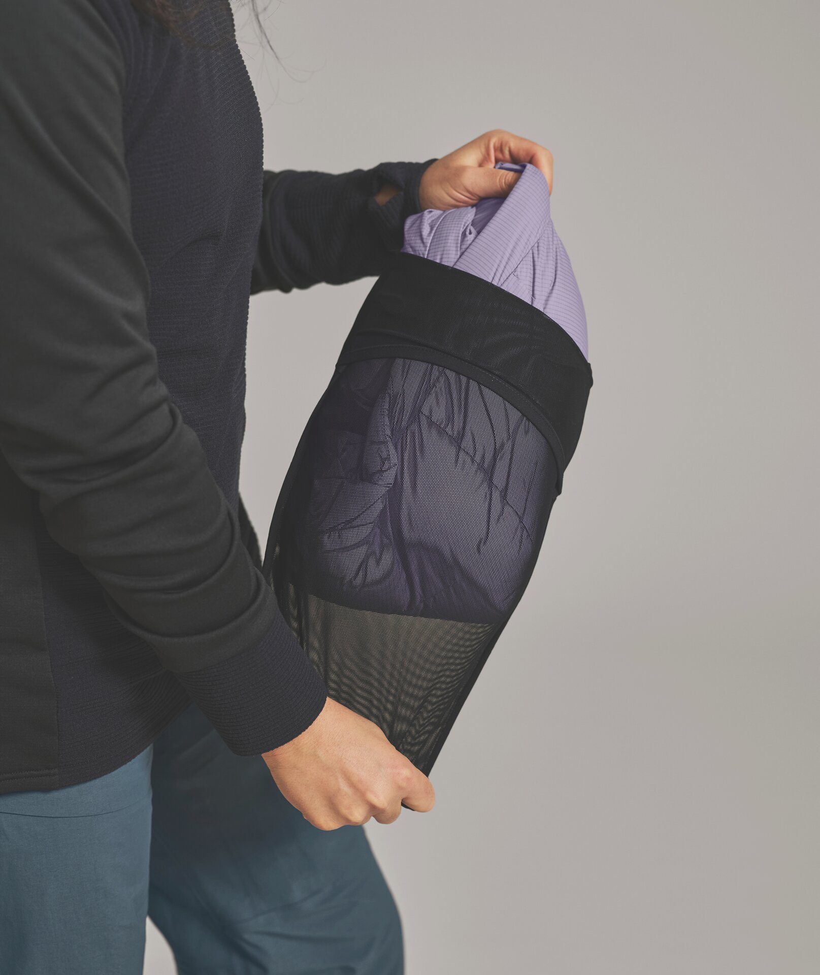 Kleidung im Netzbeutel Person packt lila Kleidung in einen schwarzen Netzbeutel. Die Person trägt einen schwarzen Pullover und grüne Hose.