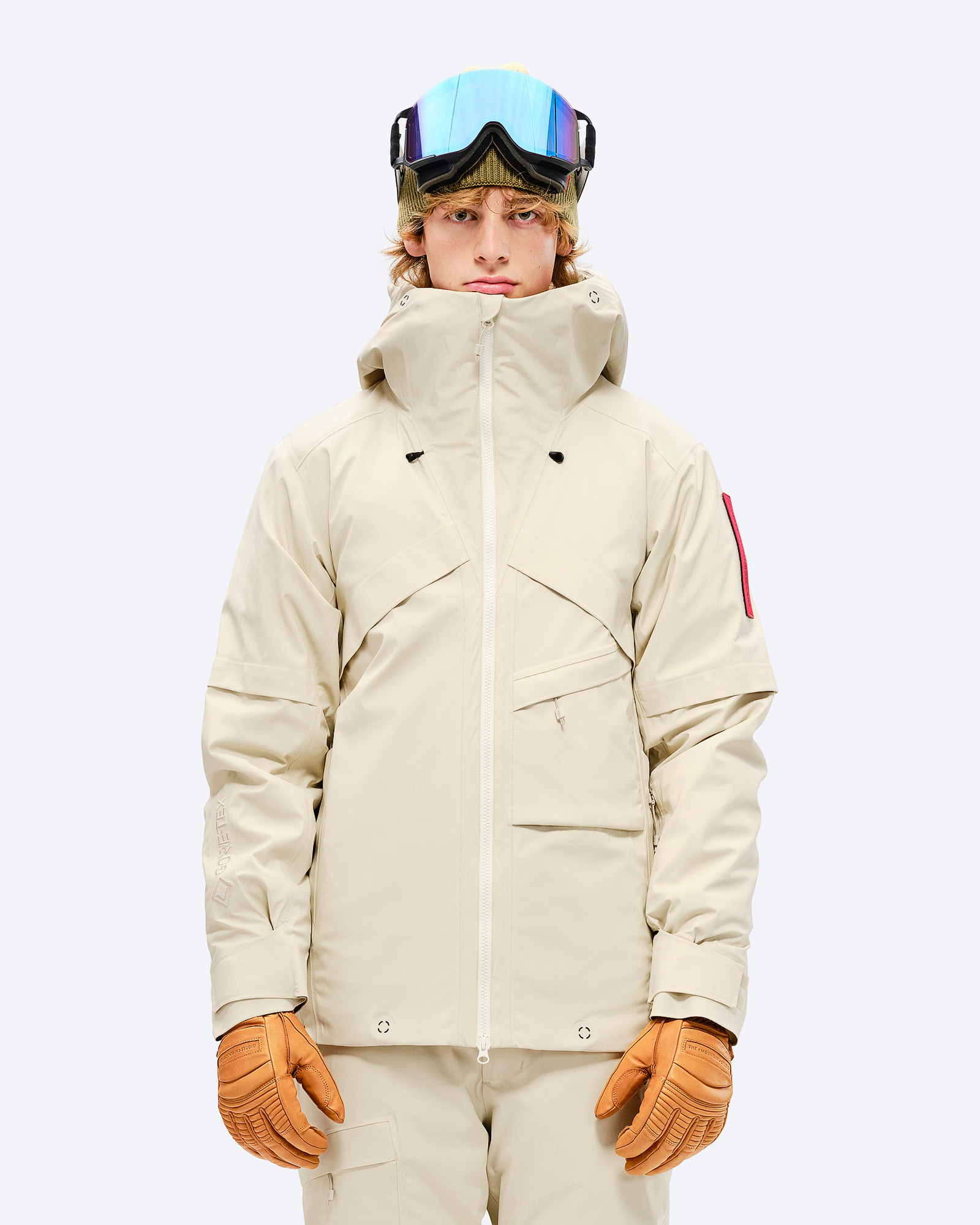 Mann in Ski-Jacke und Hose. Beige S-1 GORE-TEX 2L Stretch Insulated Jacket, Handschuhe und Skibrille.