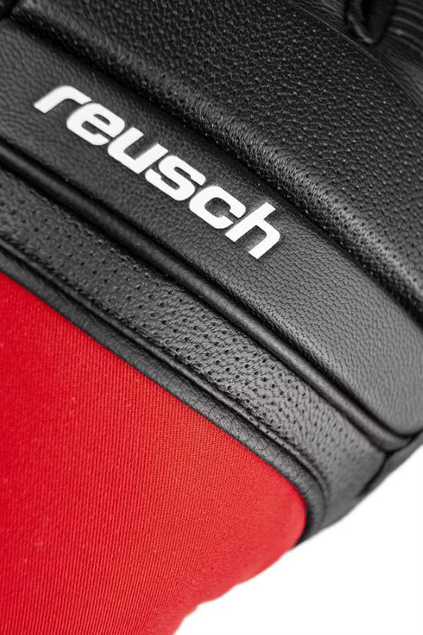 Detailaufnahme des schwarzen Reusch Marco Odermatt Handschuhs mit rotem Stoff und dem weißen Reusch-Logo.