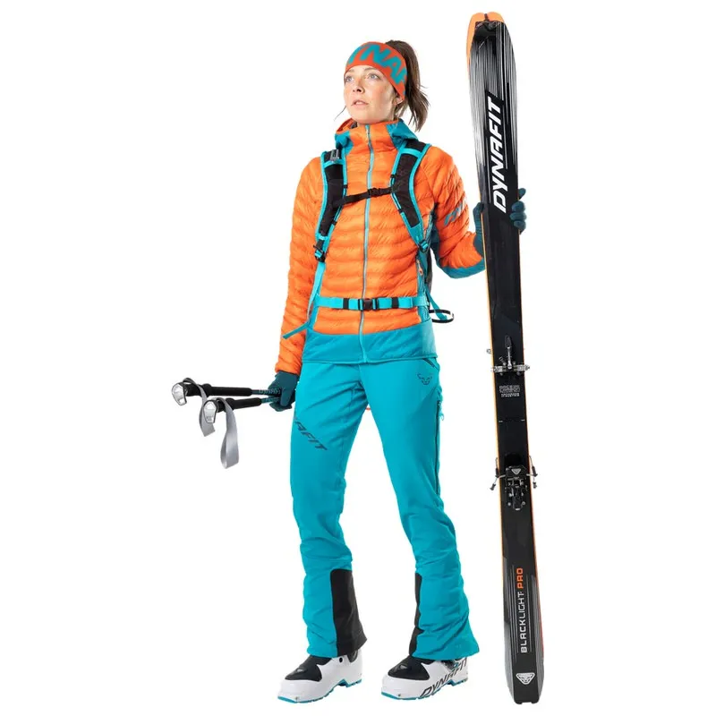 Frau in Skikleidung mit Skiern und Stöcken. Sie trägt eine petrolfarbene Dynafit TLT Touring Hose.