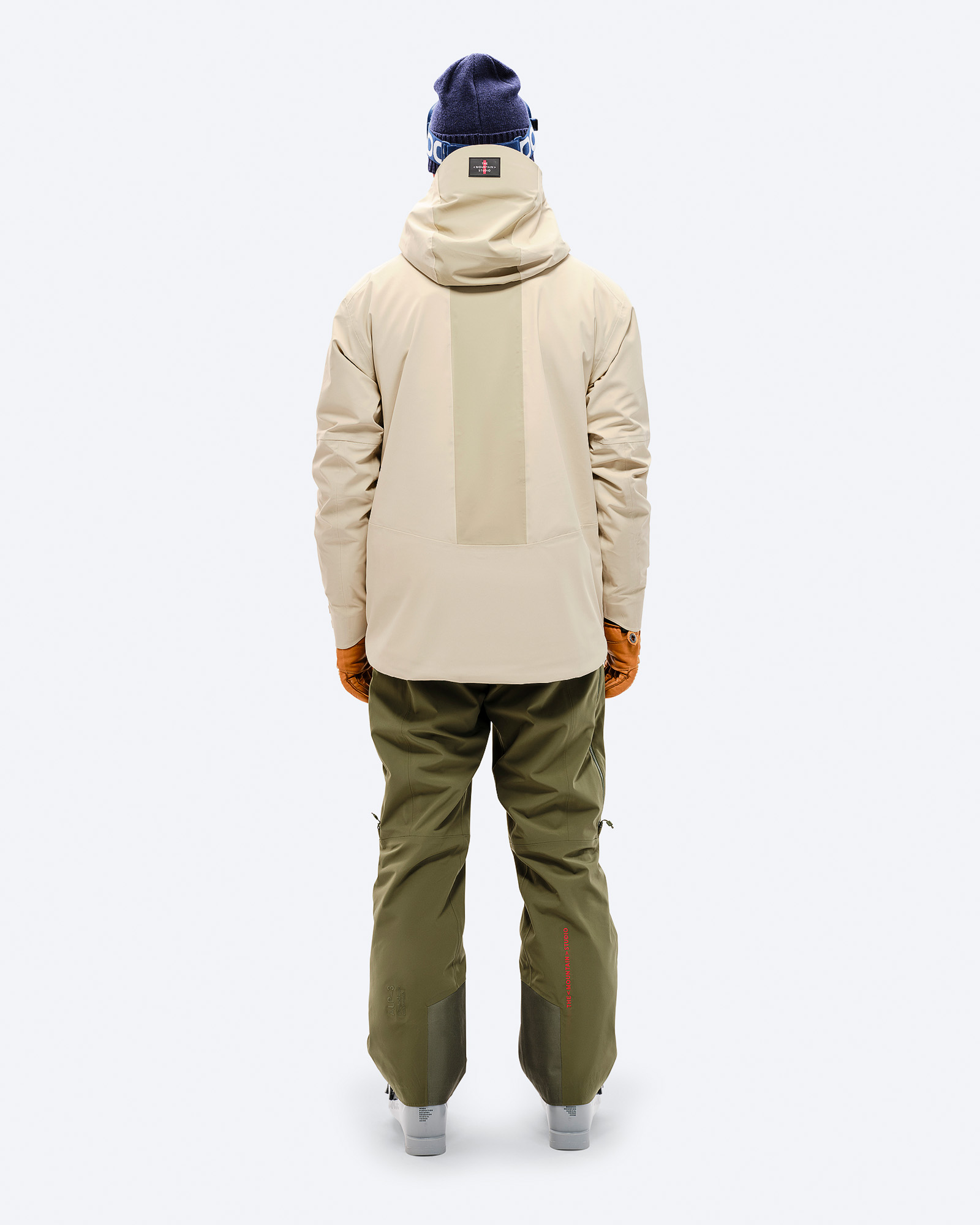 Rückansicht einer Person mit der Z-5 3L Hybrid Shell Jacket in Beige, kombiniert mit grüner Hose und braunen Handschuhen.