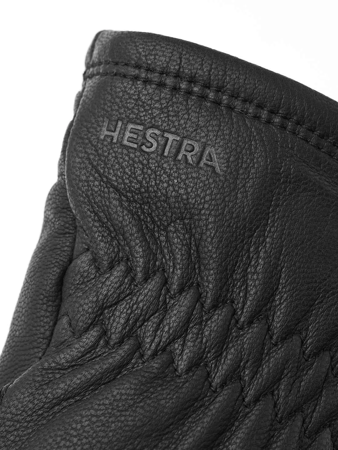 Detailaufnahme eines schwarzen Lederhandschuhs mit dem Schriftzug "HESTRA" und gesteppten Akzenten.