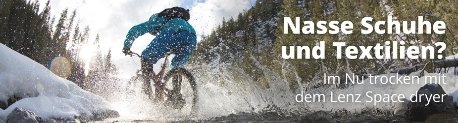 Ein Mountainbiker fährt durch einen Bach, Wasser spritzt. Text: "Nasse Schuhe und Textilien? Im Nu trocken mit dem Lenz Space dryer".