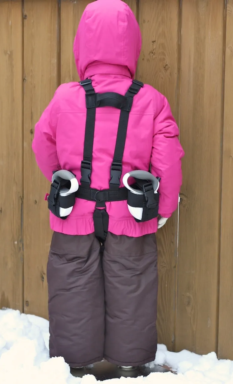 Kind mit pinker Jacke und brauner Hose trägt Lil' Ripper Gripper Skilernhilfe mit Leinen am Rücken.