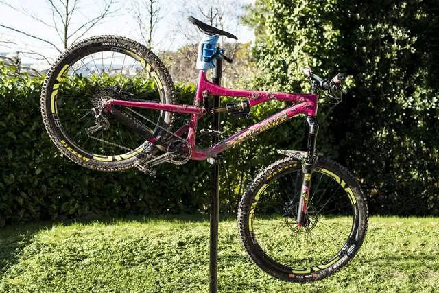Pinkes Mountainbike auf einem Montageständer im Freien, Fokus auf die Reinigung vor dem nächsten Einsatz.