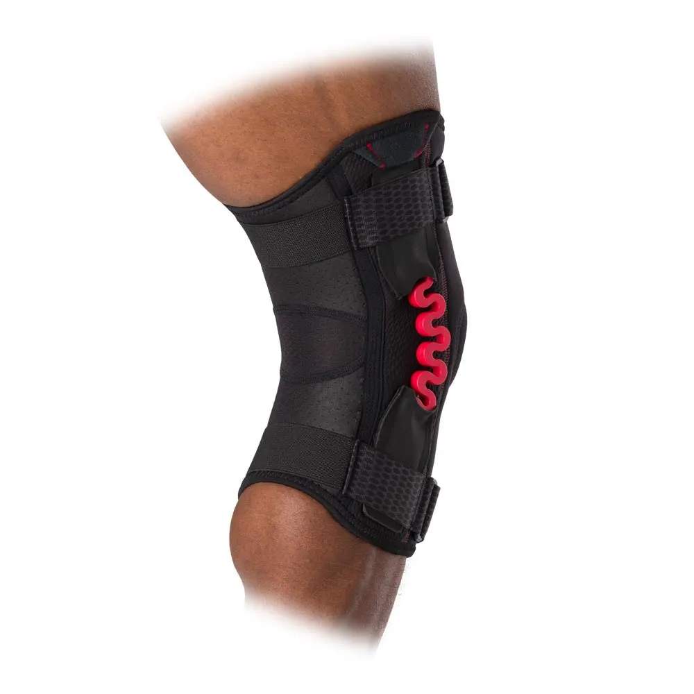Nahaufnahme einer McDavid NRG Kniebandage mit roter Federung am Knie eines Menschen. Die Bandage ist schwarz und hat verstellbare Gurte.