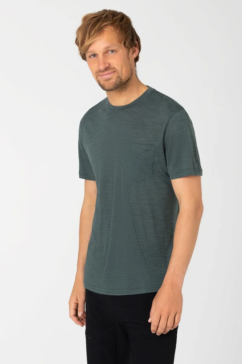 Mann trägt meliertes, petrolfarbenes T-Shirt mit Brusttasche und schwarze Hose. Lässig, Blick zur Seite.