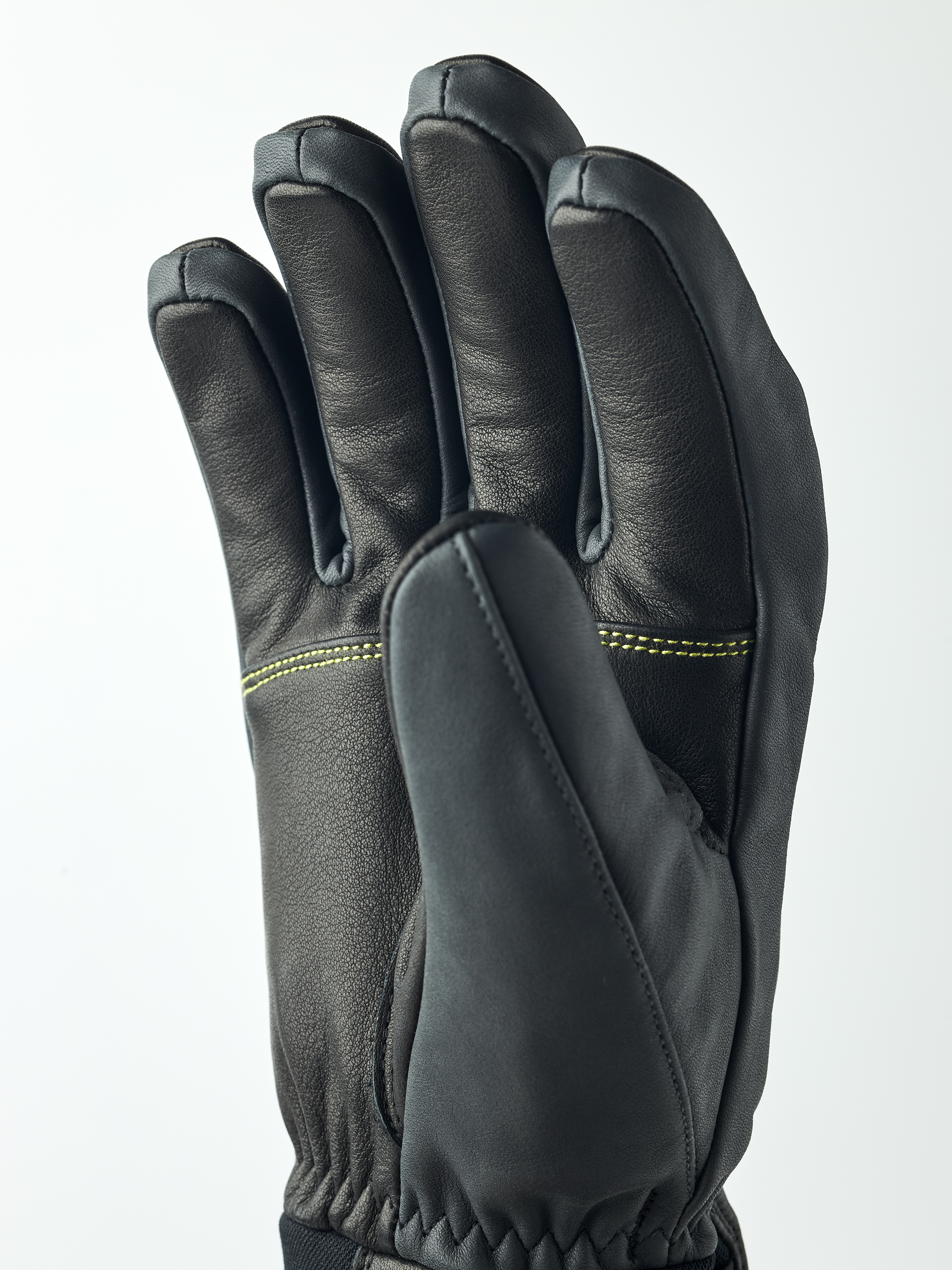 Schwarzer Hestra Omni Trigger Handschuh von Nahem, die Hand ist leicht geöffnet und zeigt die Finger. Gelbe Nähte sind sichtbar.