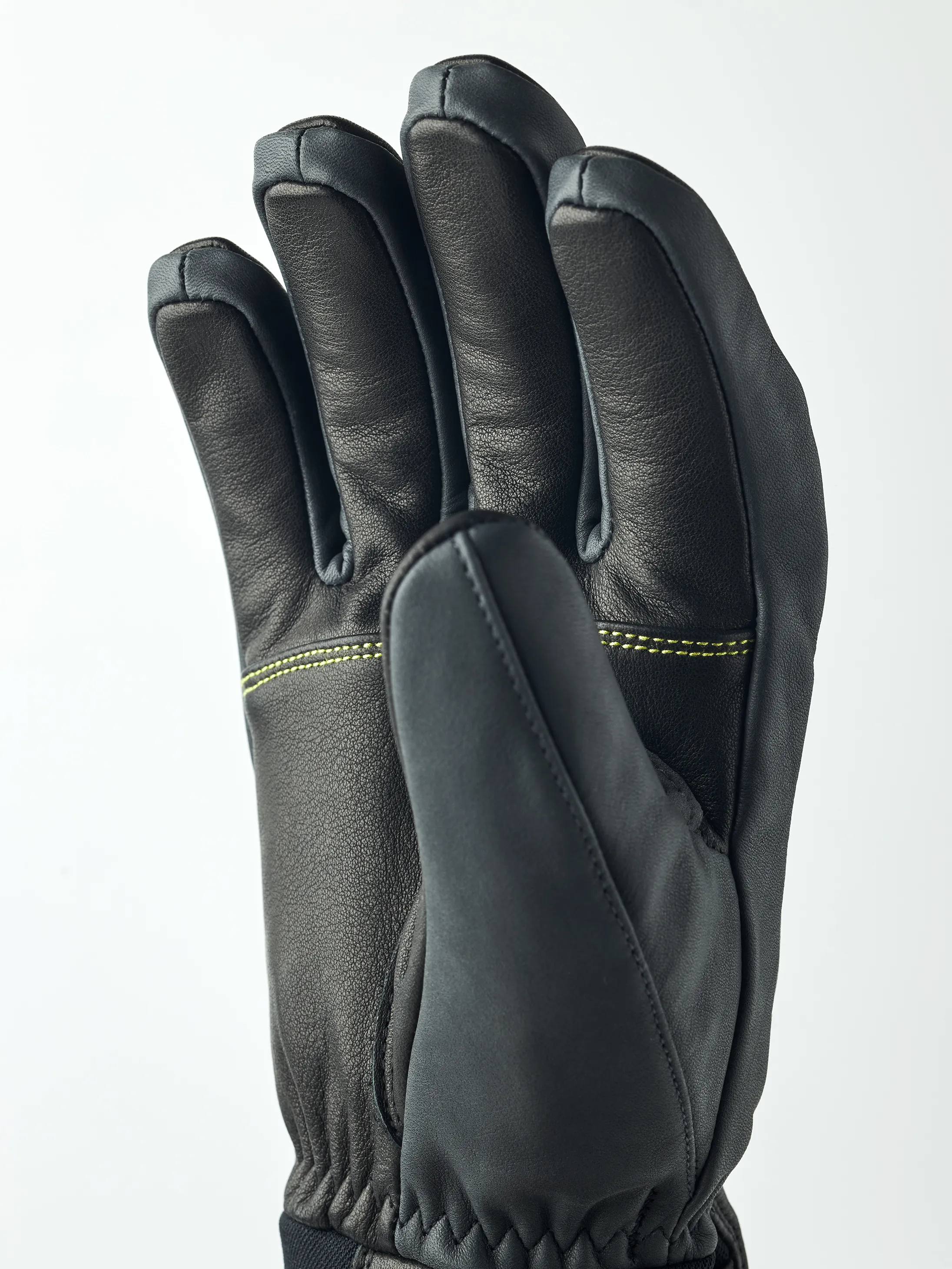 Schwarzer Hestra Omni Trigger Handschuh von Nahem, die Hand ist leicht geöffnet und zeigt die Finger. Gelbe Nähte sind sichtbar.