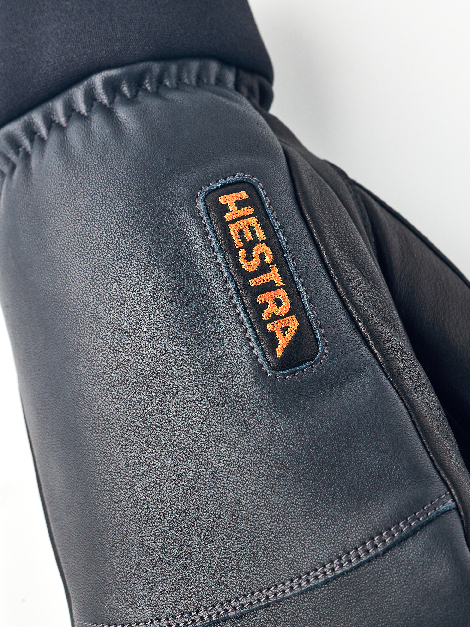 Detailaufnahme eines Hestra Army Leather Wool Terry Fäustlings mit orangem Hestra-Logo.