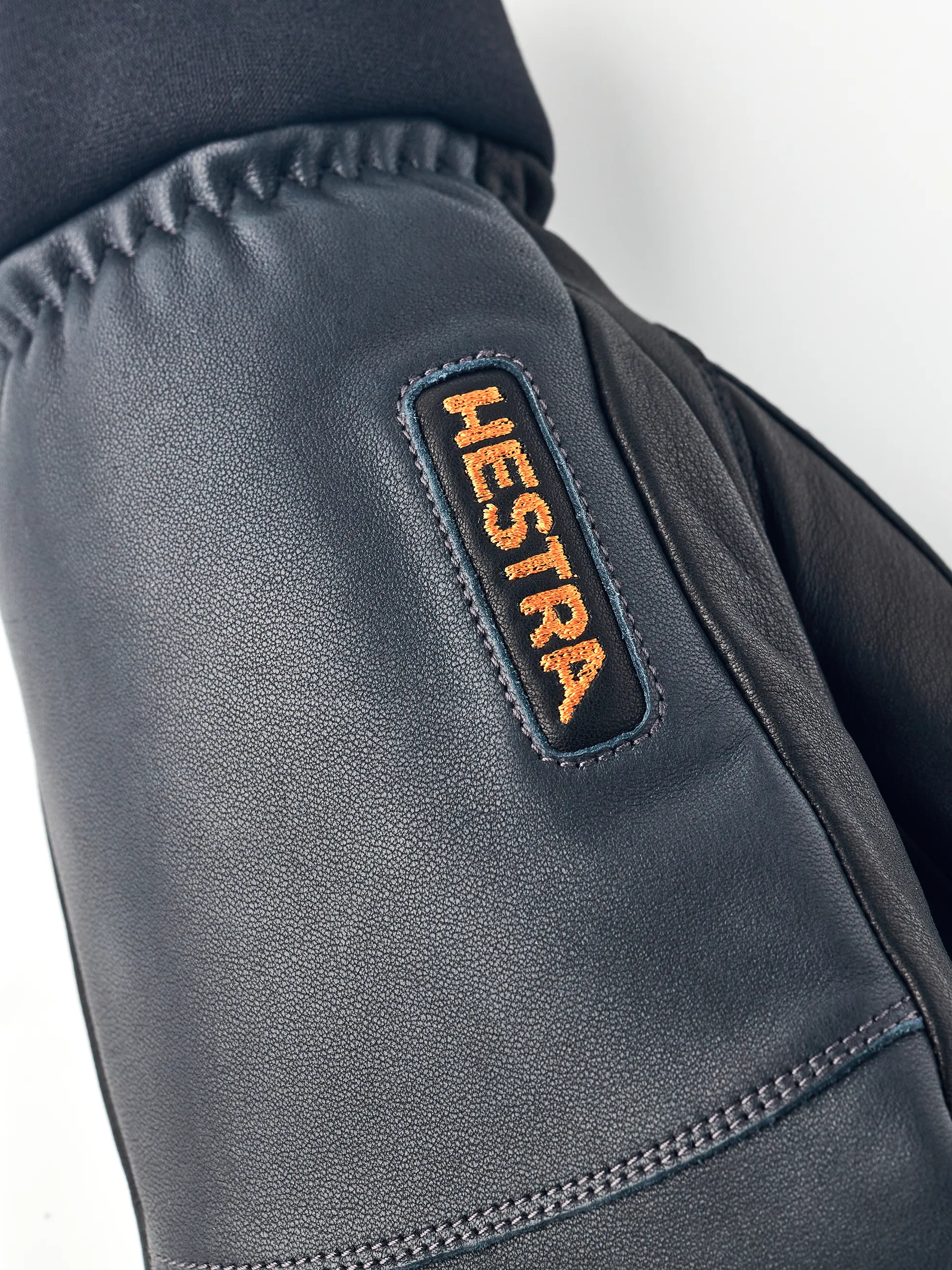 Detailaufnahme eines Hestra Army Leather Wool Terry Fäustlings mit orangem Hestra-Logo.