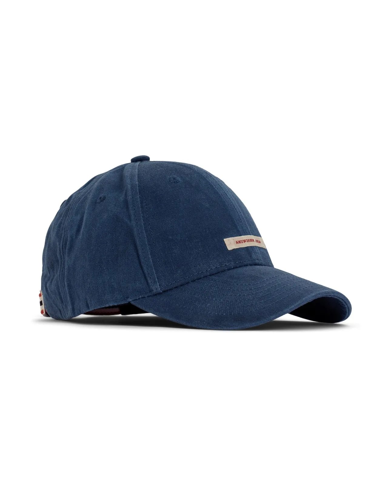 Eine dunkelblaue Amundsen Waxed Cotton Cap, auf weißem Grund, mit kleinem, beigefarbenem Logo über dem Schirm. Der Stoff der Kappe ist gewachst. Die Kappe ist auf der Seite fotografiert, so dass Form gut sichtbar ist.