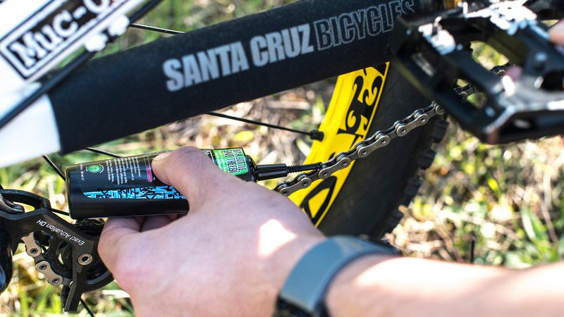 Fahrrad-Kette Pflege Fahrrad-Kette wird mit Muc-Off Wet Lube geschmiert. Flasche mit grünem Etikett. Fahrrad-Details sichtbar.