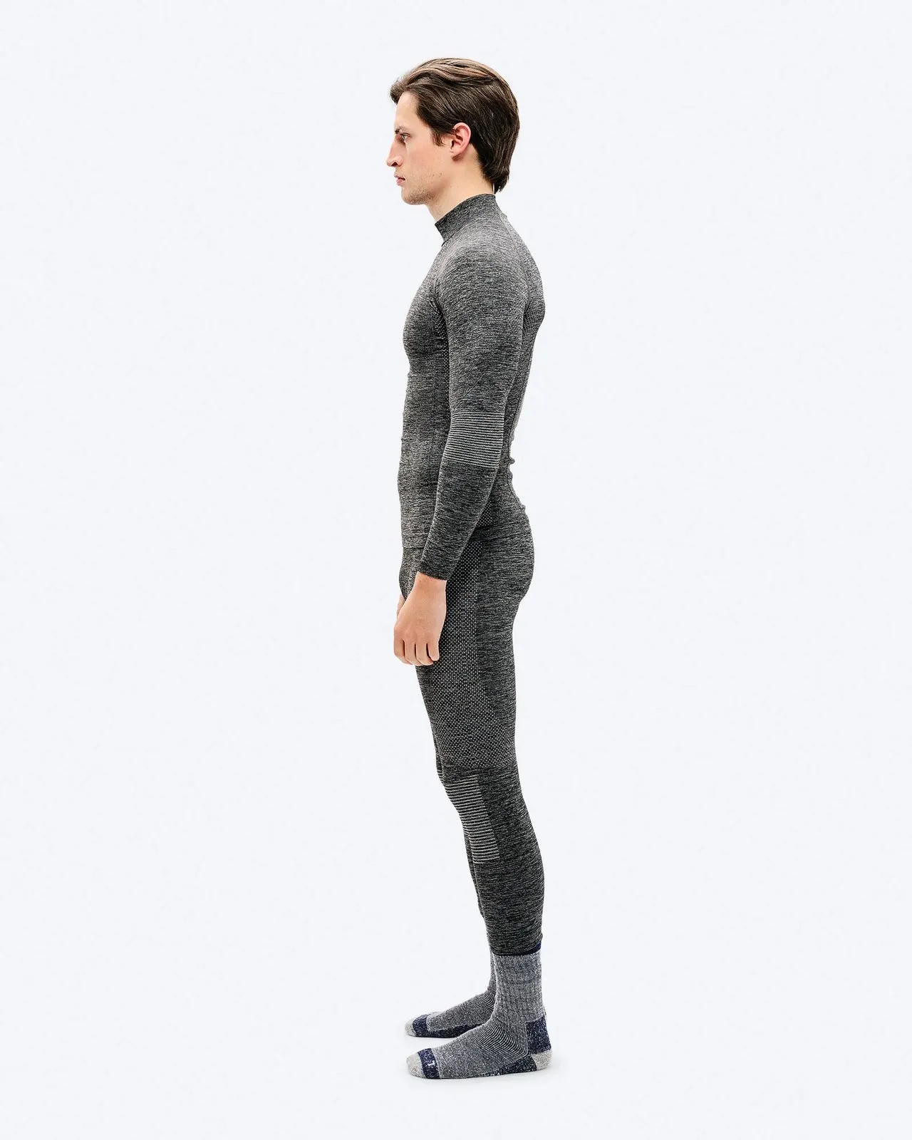 Mann in grauer, eng anliegender Sportbekleidung im Profil vor weißem Hintergrund. Er trägt graue Socken.