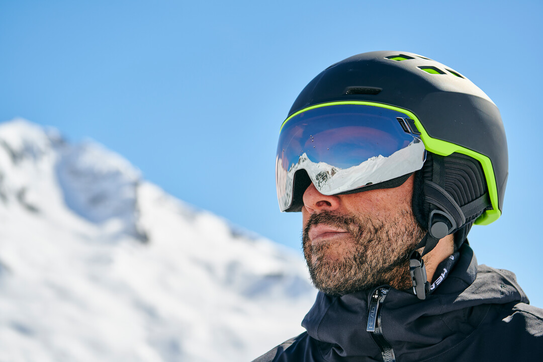 HEAD Radar Visierhelm – Innovation und Komfort für Skifahrer Mann mit Bart, Skihelm und reflektierender Brille. Im Hintergrund verschwommene, schneebedeckte Berge und blauer Himmel.