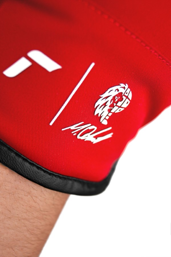 Rotes Kleidungsstück mit Logo Nahaufnahme eines roten Kleidungsstücks mit weißem Logo, Strich und Schriftzug am Ärmel mit schwarzem Saum.