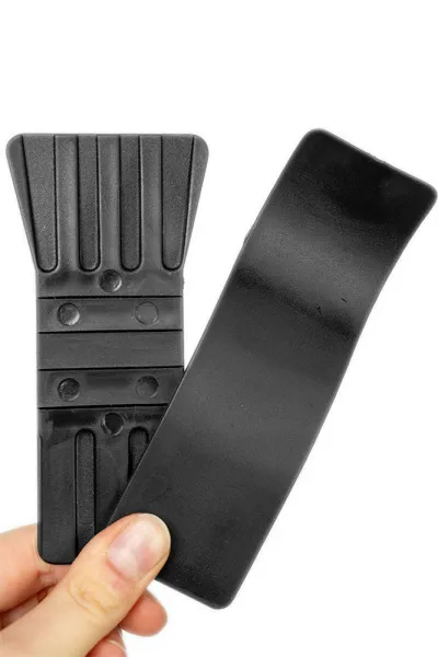 Eine Hand hält einen schwarzen, gerippten Kunststoffgegenstand neben einem glatten, gebogenen Kunststoffstreifen.