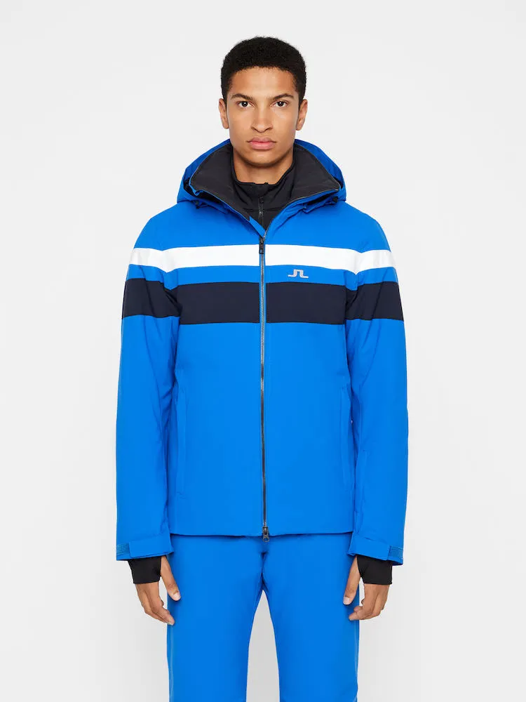 Blaues J.Lindeberg Franklin Skijacke mit weißen und dunklen Streifen, von vorne an einem Model getragen.