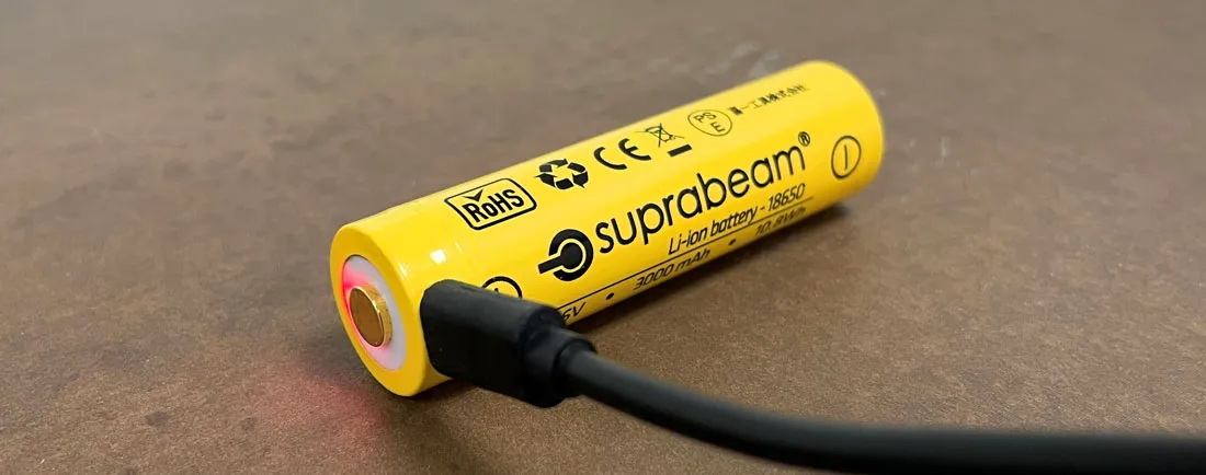 Gelbe Suprabeam 18650 Li-Ion Batterie mit USB-Kabel zum Aufladen auf brauner Oberfläche.