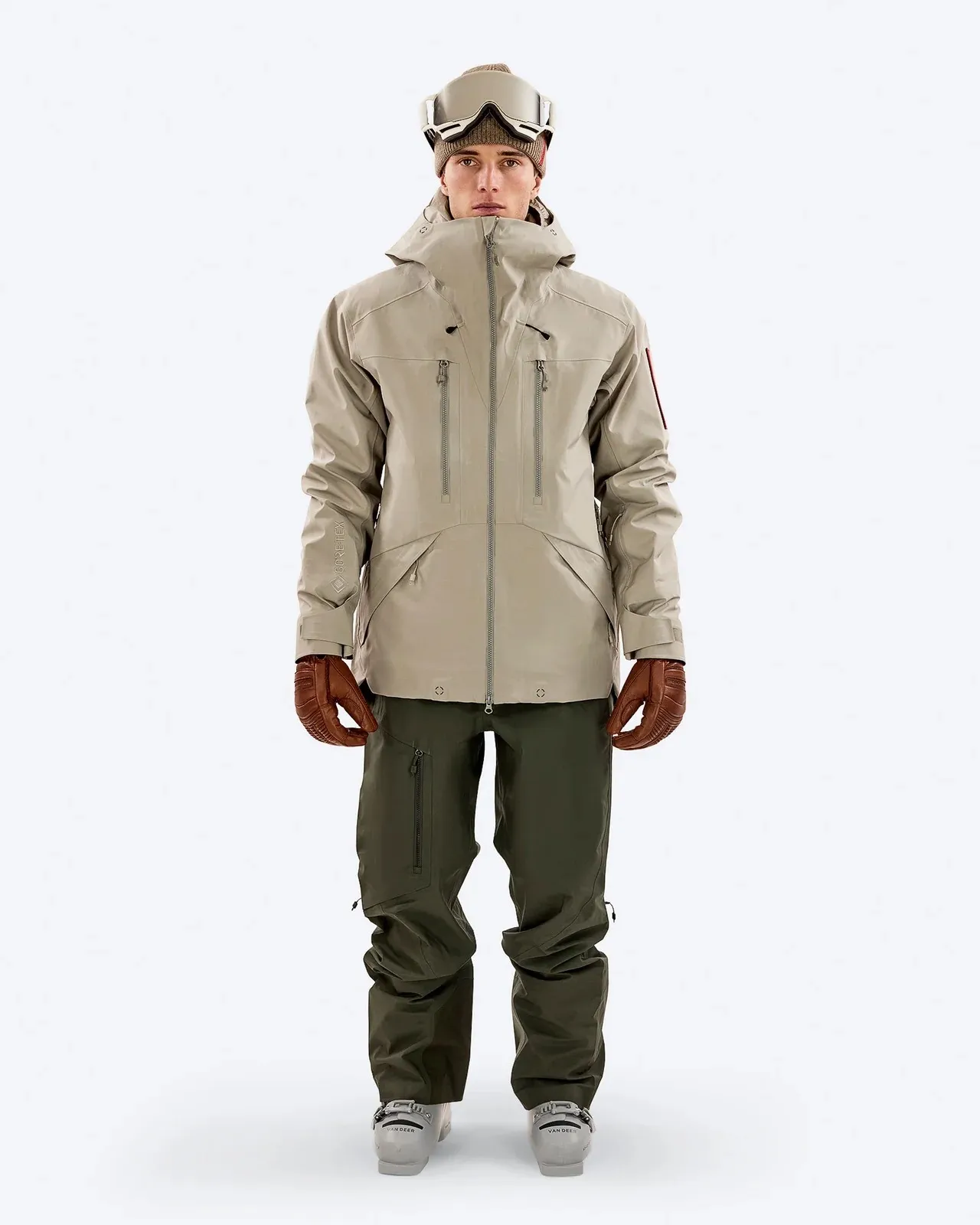 Model mit Z-2 EPE 3L Jacket Seneca Rock, Skibrille und Handschuhen. Die Jacke ist beige, die Hose ist grün.