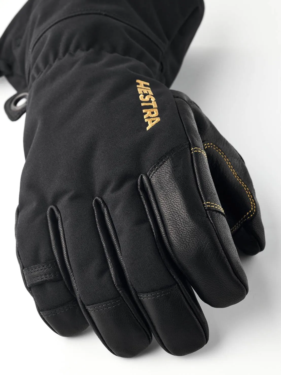 Nahaufnahme eines schwarzen Hestra Gore-Tex Fünffingerhandschuhs mit Lederdetails und goldener Hestra-Aufschrift.