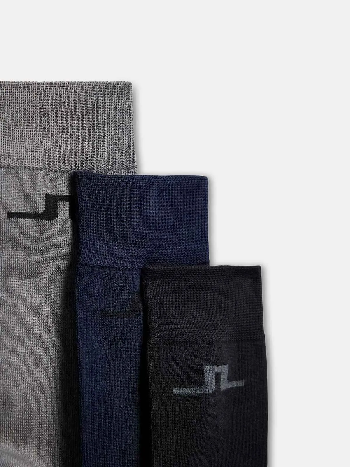 Drei J.Lindeberg Socken im 3er-Pack in Grau, Dunkelblau und Schwarz, mit dem Bridge-Logo am Schaft.
