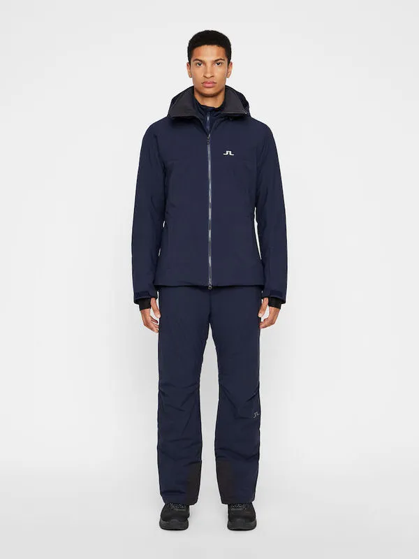 Ein Mann trägt navyfarbene J.Lindeberg Truulli Skihose und passende Jacke.