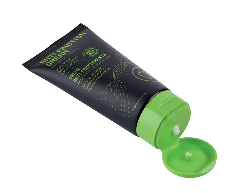 Schwarze Tube Anti-Friction Creme mit grünem Verschluss und einem Tropfen Creme, die aus der Tube kommt, vor weißem Hintergrund.