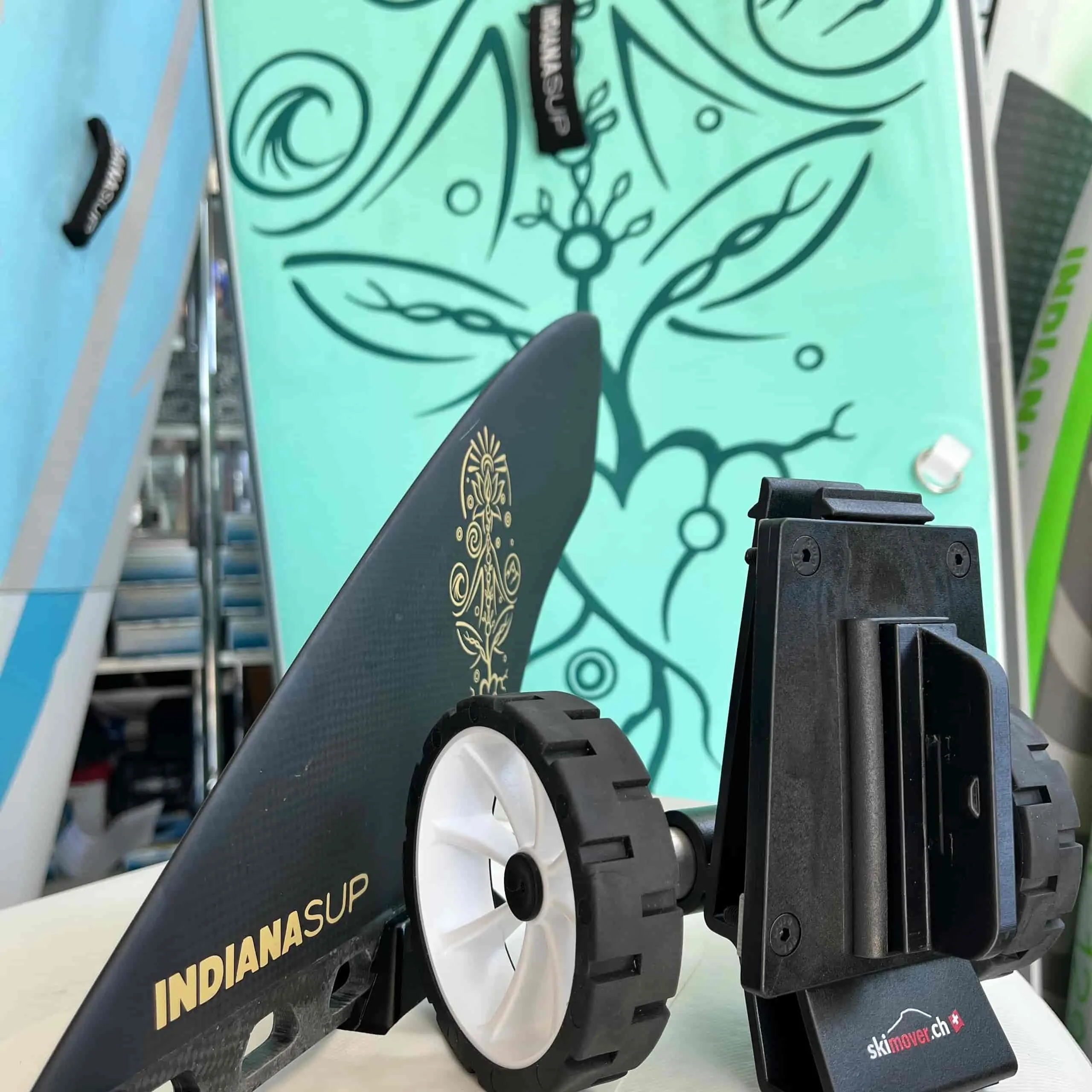 SUPmover Räder, mit schwarzem Halter, weisser Felge, neben einer Finne und einem SUP Board.