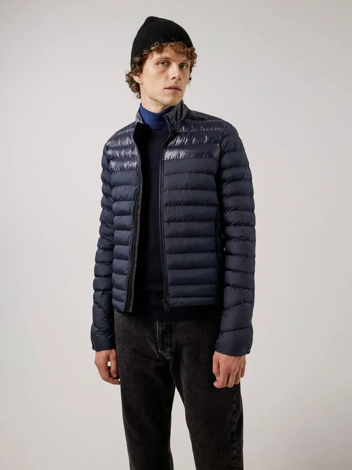 Ein Mann mit Mütze trägt eine dunkelblaue, gesteppte Rick Light Jacket über einem Rollkragenpullover.