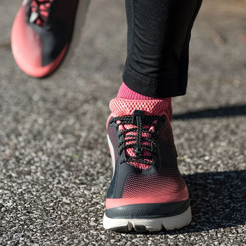 Nahaufnahme von Laufschuhen mit schwarzen, elastischen Schnürsenkeln und pinken Socken auf Asphalt.