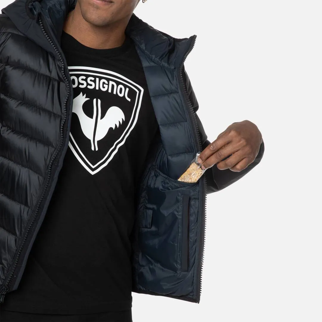 Geöffnete, gesteppte, dunkelblaue Rossignol Hoodie Jacke; Mann nimmt Riegel aus Innentasche.