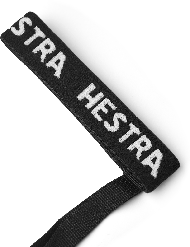 Schwarzes Textilband "STRA HESTRA" Schwarzes Textilband mit weißem "STRA HESTRA" Schriftzug und schwarzem Band an einem Ende, auf weißem Grund.
