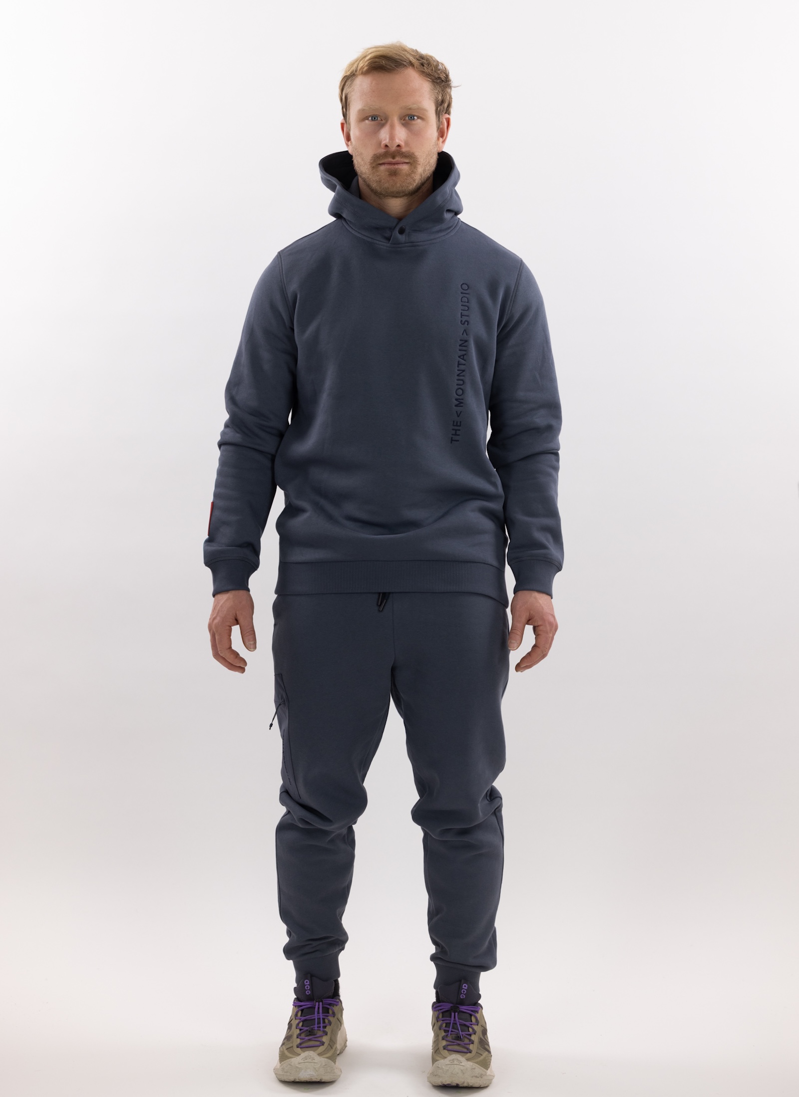 Mann in grauer Z-5 3L Hybrid Shell Jacket und passender Hose von The Mountain Studio vor weißem Hintergrund.