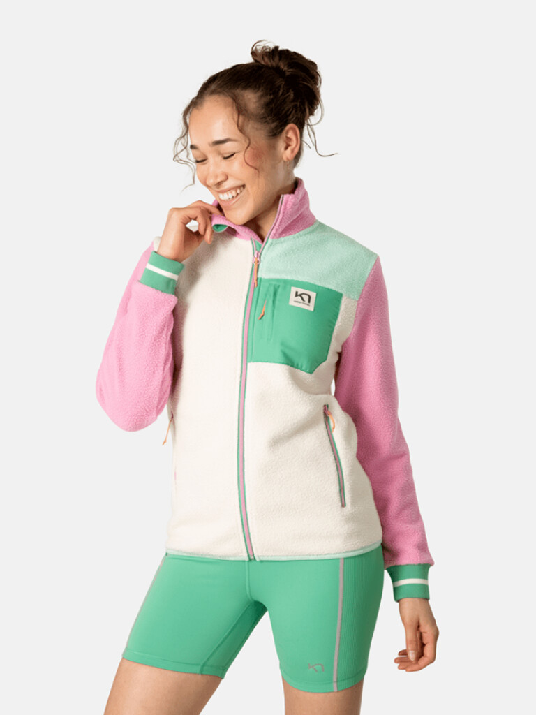 Lächelnede Frau trägt Kari Traa Rothe Midlayer in Weiß, Rosa und Grün, dazu passende Shorts.