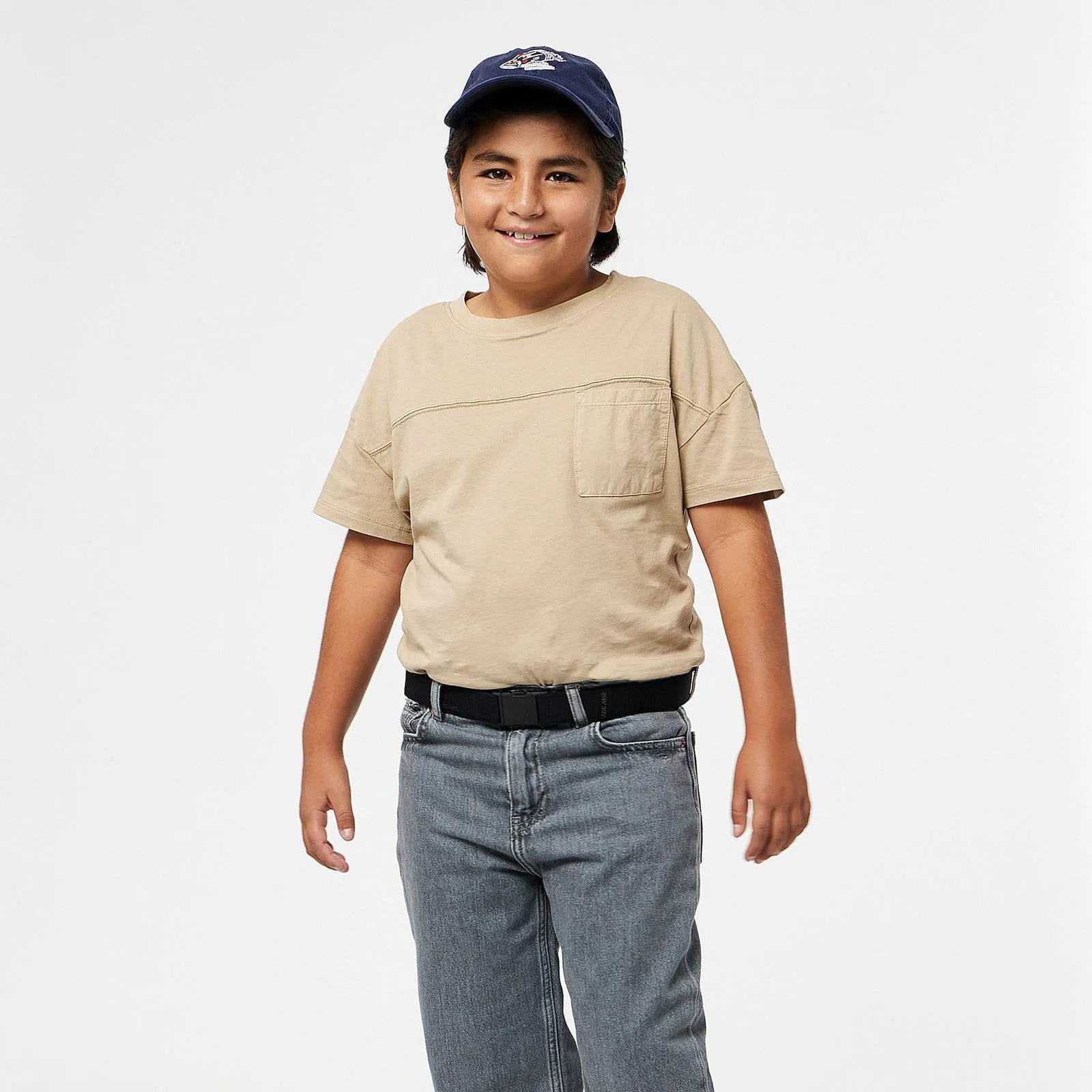 Kind mit blauem Basecap und beigem T-Shirt, trägt einen schwarzen Arcade Atlas Gürtel zu grauen Jeans.