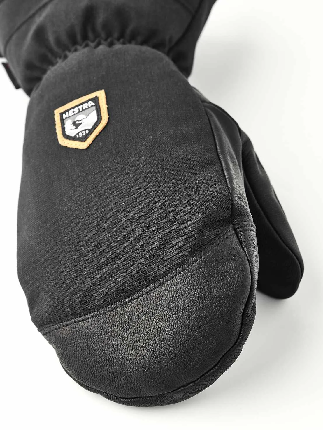 Nahaufnahme eines schwarzen Fäustlings aus Stoff und Leder mit Hestra-Logo.