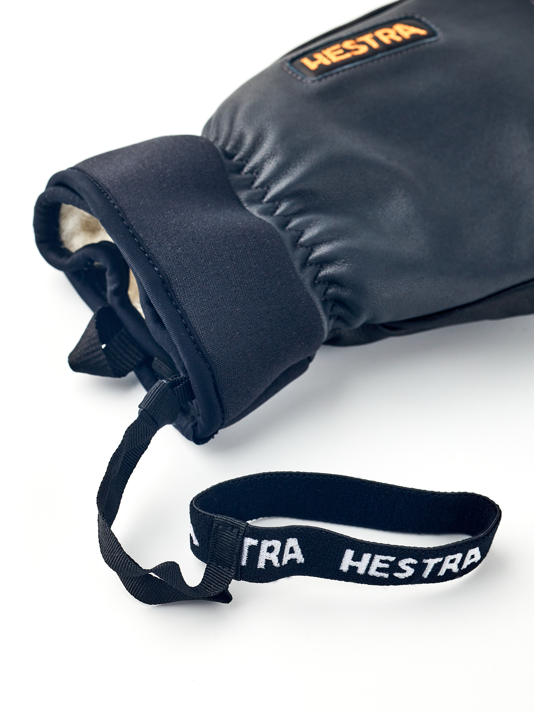 Nahaufnahme von Hestra Army Leather Wool Terry Fäustling mit Handgelenkschlaufe auf weißem Hintergrund.