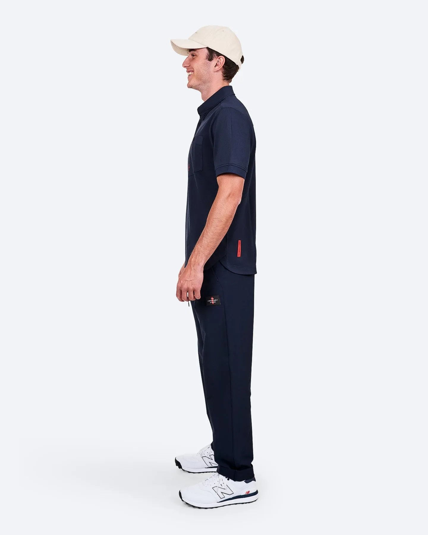 Mann von der Seite, in marineblauem Polohemd, Jogginghose und weißen Turnschuhen, mit beiger Kappe.