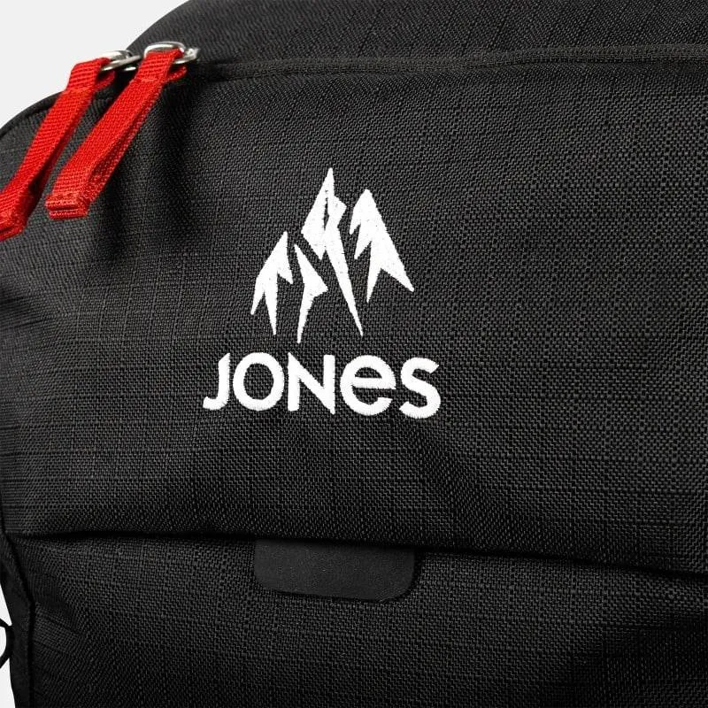 Detailansicht eines schwarzen Jones Further 25L Rucksacks mit weißem Logo und roten Reißverschlüssen.