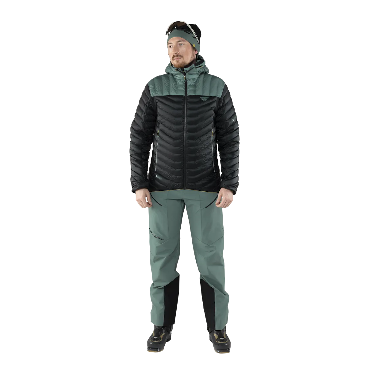 Mann in Daunenjacke und Skitourenhose, vor weißem Hintergrund. Die Jacke ist schwarz und grün.