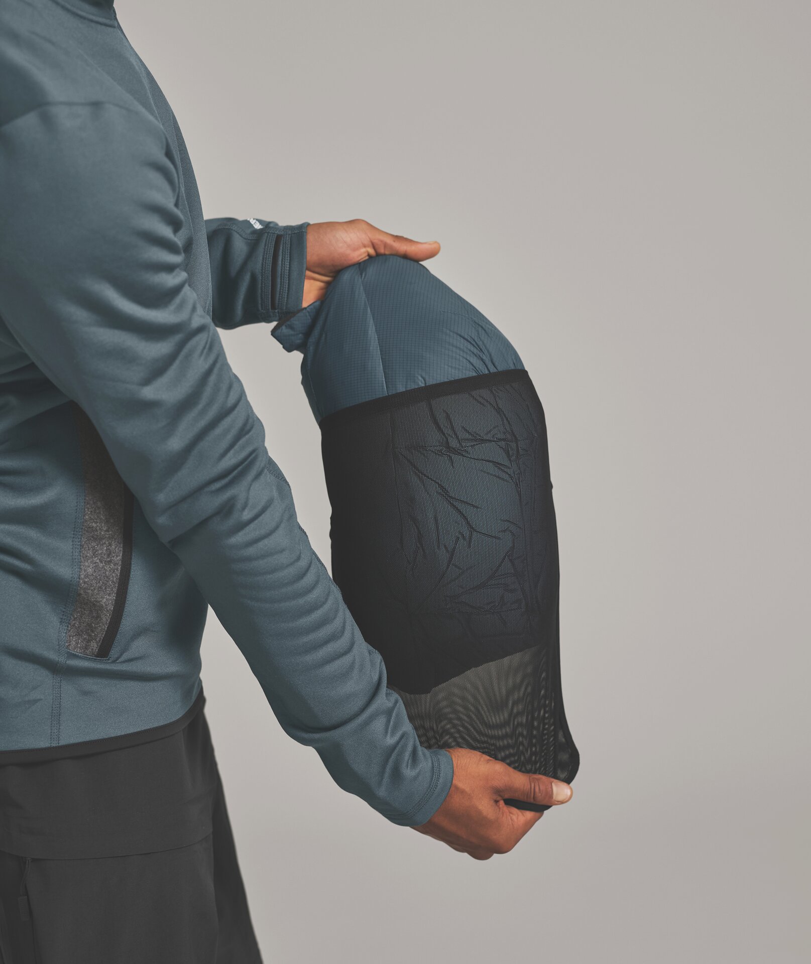 Schlafsack in Netztasche Person hält Schlafsack in einer schwarzen Netztasche vor hellgrauem Hintergrund.