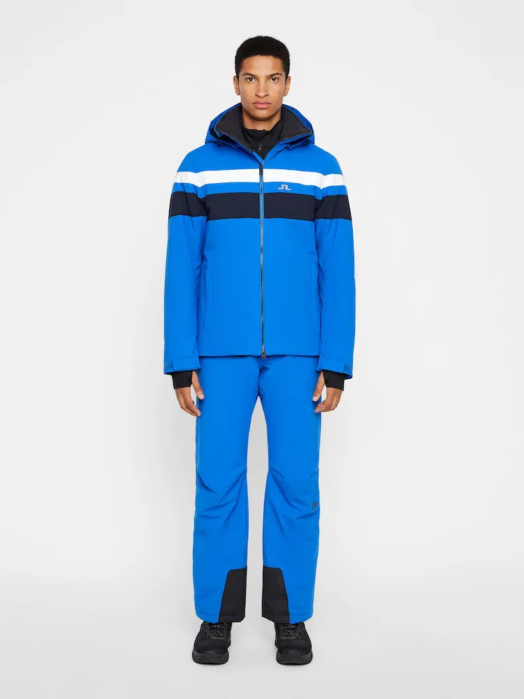 Ein Mann trägt eine blaue J.Lindeberg Franklin Skijacke und Hose mit weißen und marineblauen Streifen.