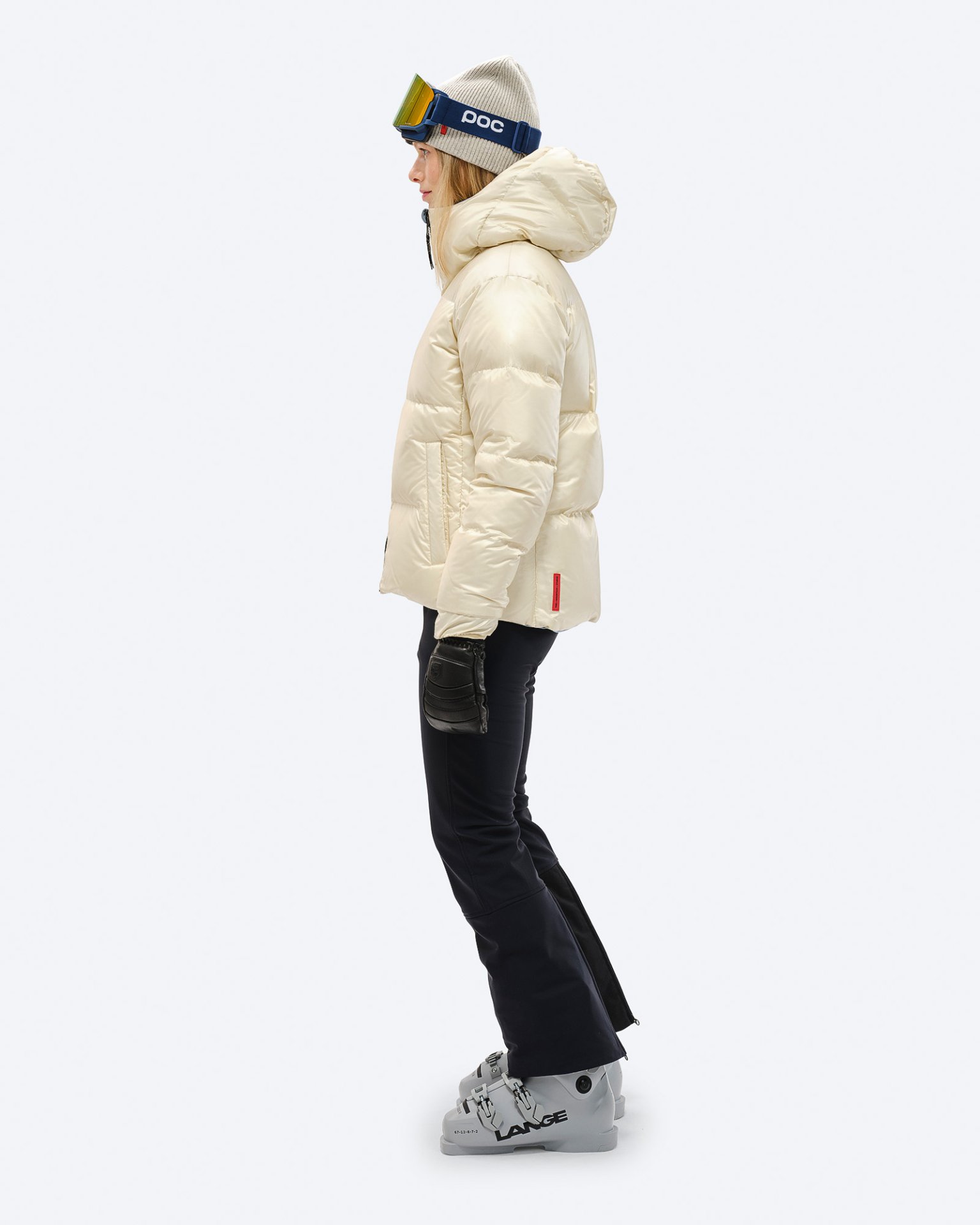 Person in Skikleidung, trägt eine Daunenjacke in Castle Wall Farbe, Mütze und Skibrille. Ski sind angezogen.