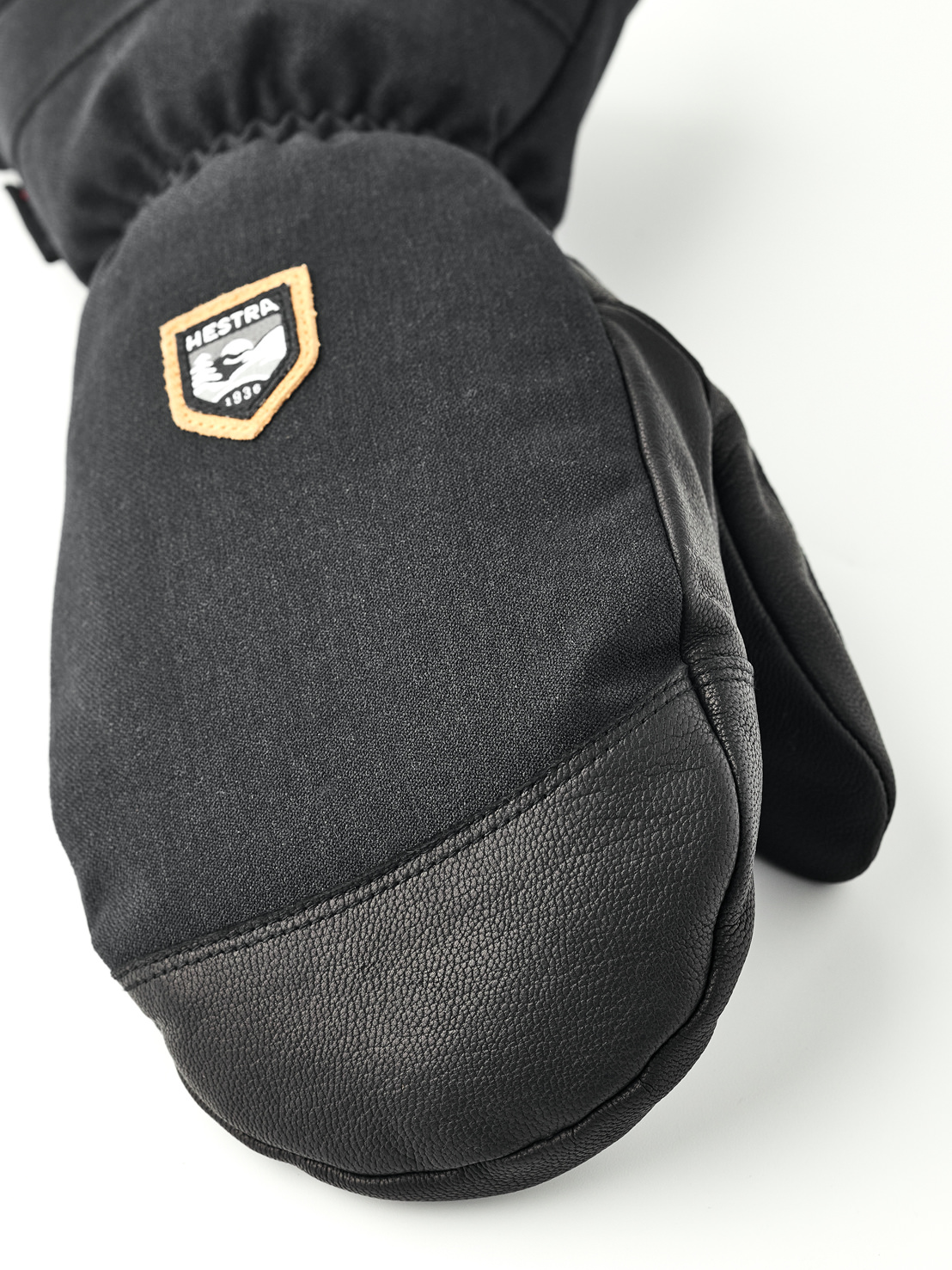 Nahaufnahme eines schwarzen Fäustlings aus Stoff und Leder mit Hestra-Logo.