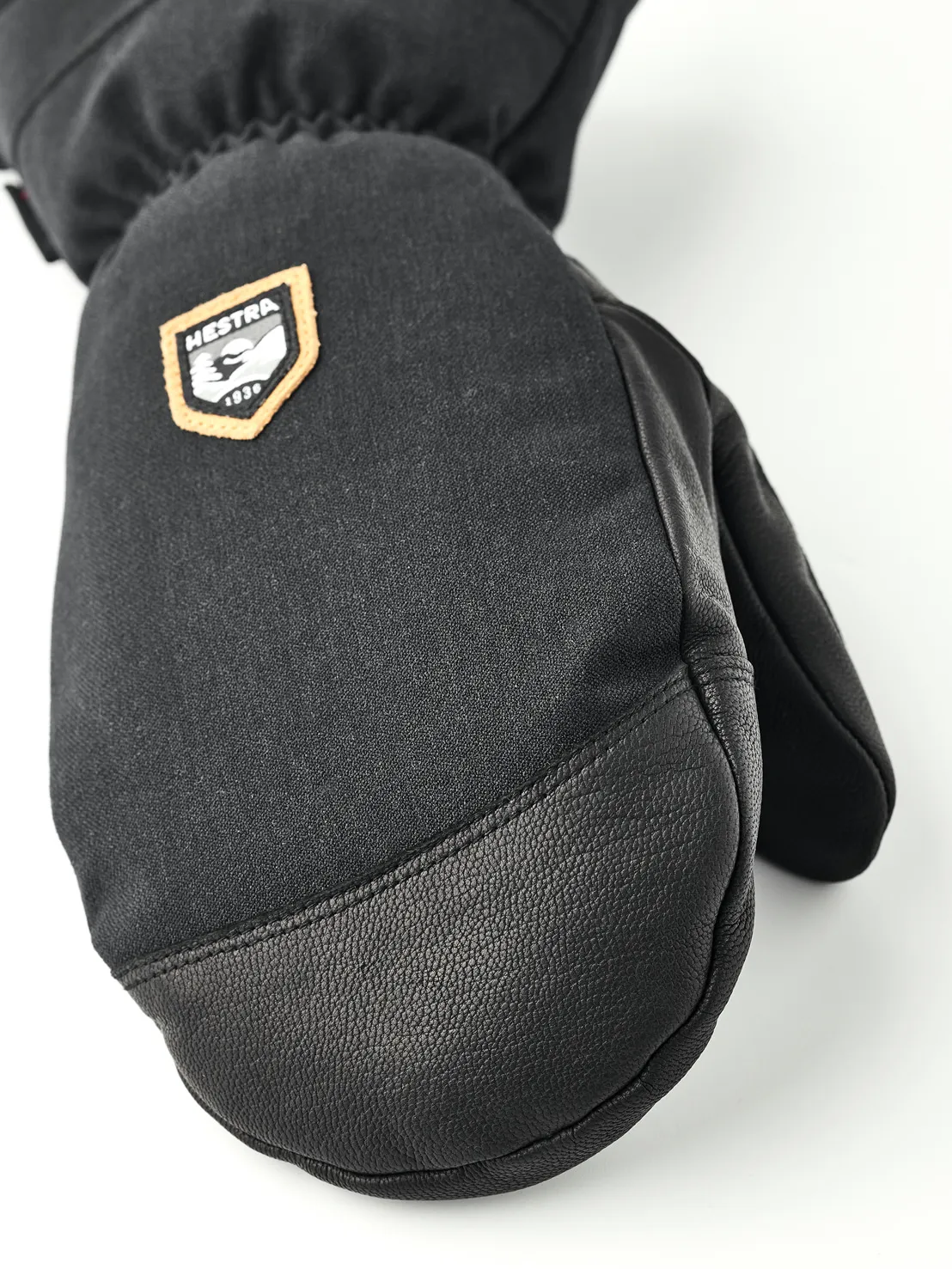 Nahaufnahme eines schwarzen Fäustlings aus Stoff und Leder mit Hestra-Logo.