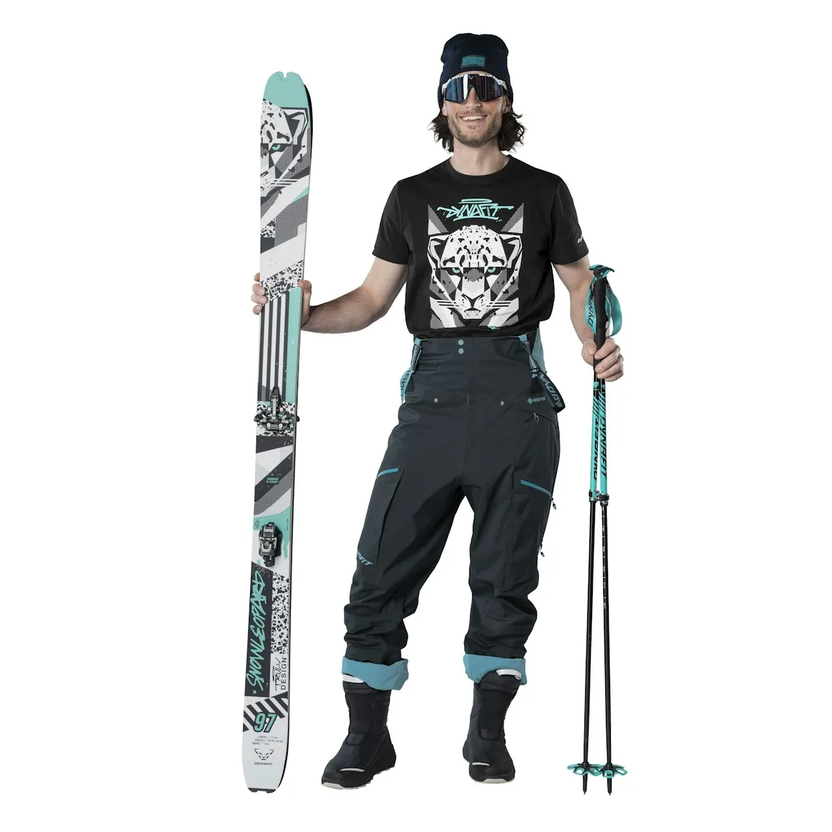 Skibekleidung: Mann mit Ski, Skistöcken, Mütze, Brille und T-Shirt mit Leopardenmotiv. Dunkle Skihose.